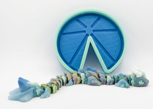 A blue and mint green silicone mold with a wedge-shaped cutout, shown with colorful blue, green, and gray clay pieces arranged in front on a white background.