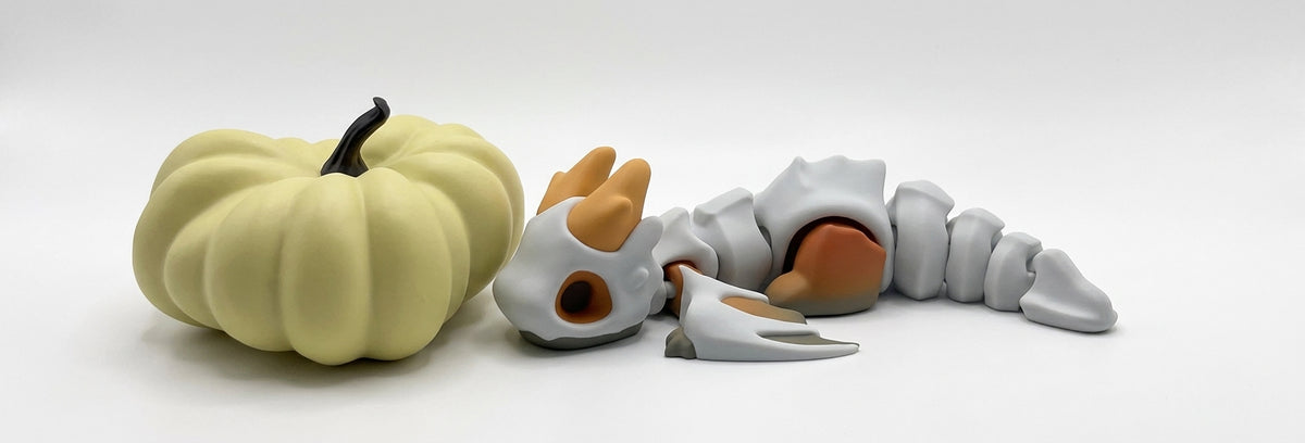 A pale yellow pumpkin-shaped object with a black stem sits beside a gray skeletal creature figure with orange-brown hands and feet on a white studio background.
