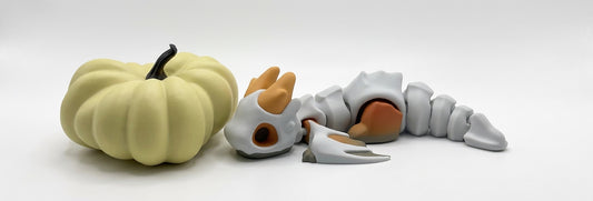 A pale yellow pumpkin-shaped object with a black stem sits beside a gray skeletal creature figure with orange-brown hands and feet on a white studio background.