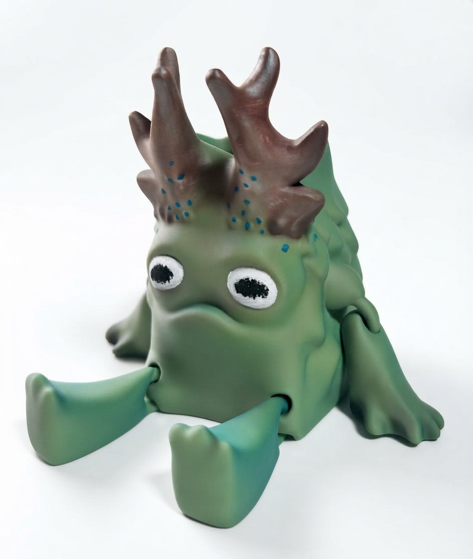 A green monster figurine with large white eyes, brown antler-like horns, and four legs, photographed on a clean white background.